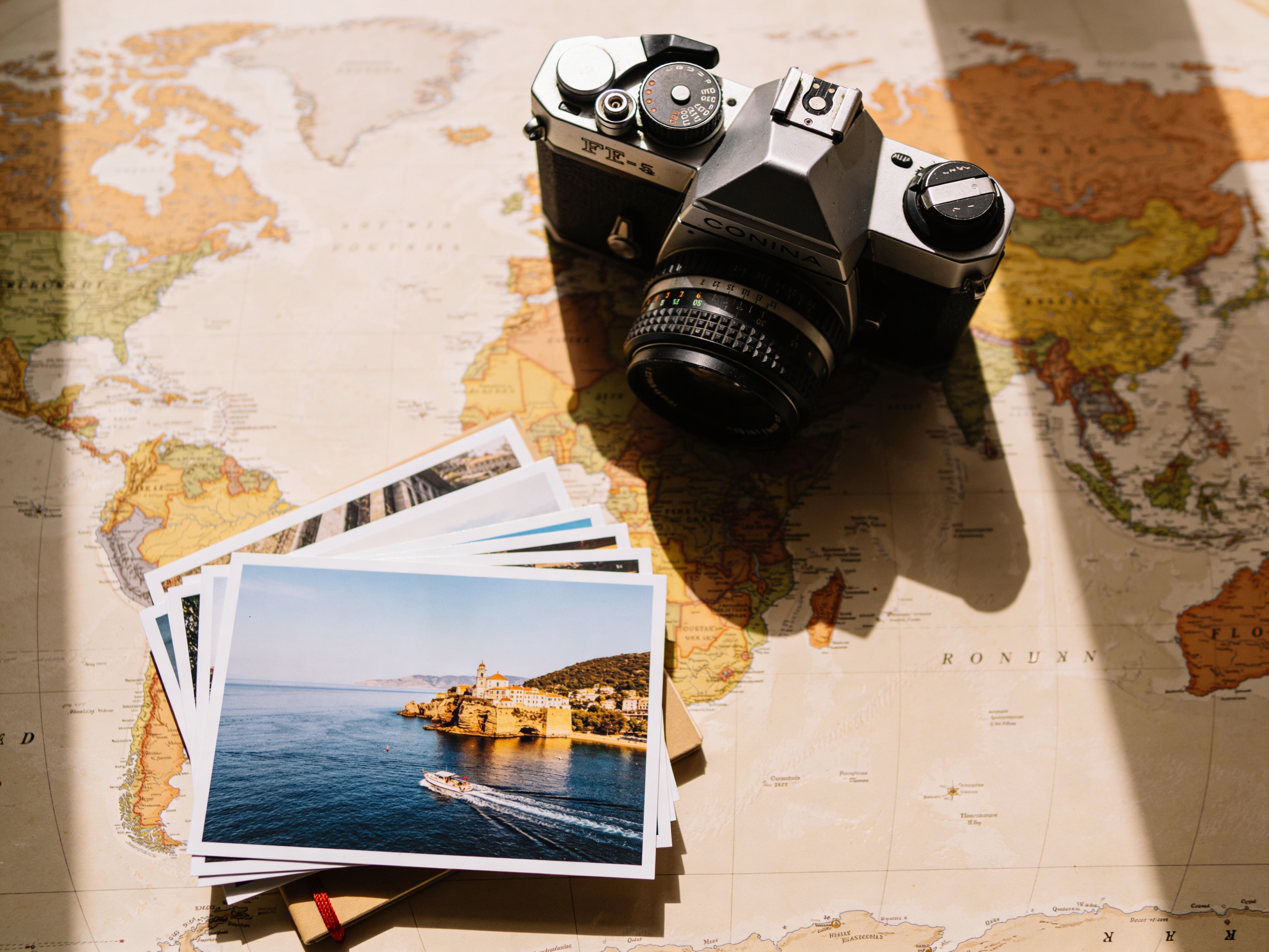 A retro film camera and a stack of postcards on a vintage world map, flat lay composition, afternoon window light, earthy color palette, travel journal aesthetic, 4:3.